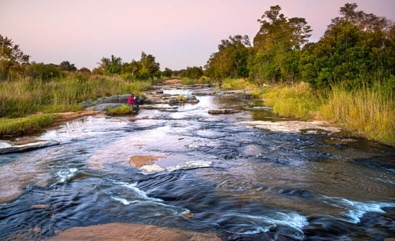 Landscape of a person reading a book while sitting on a rock in a river
